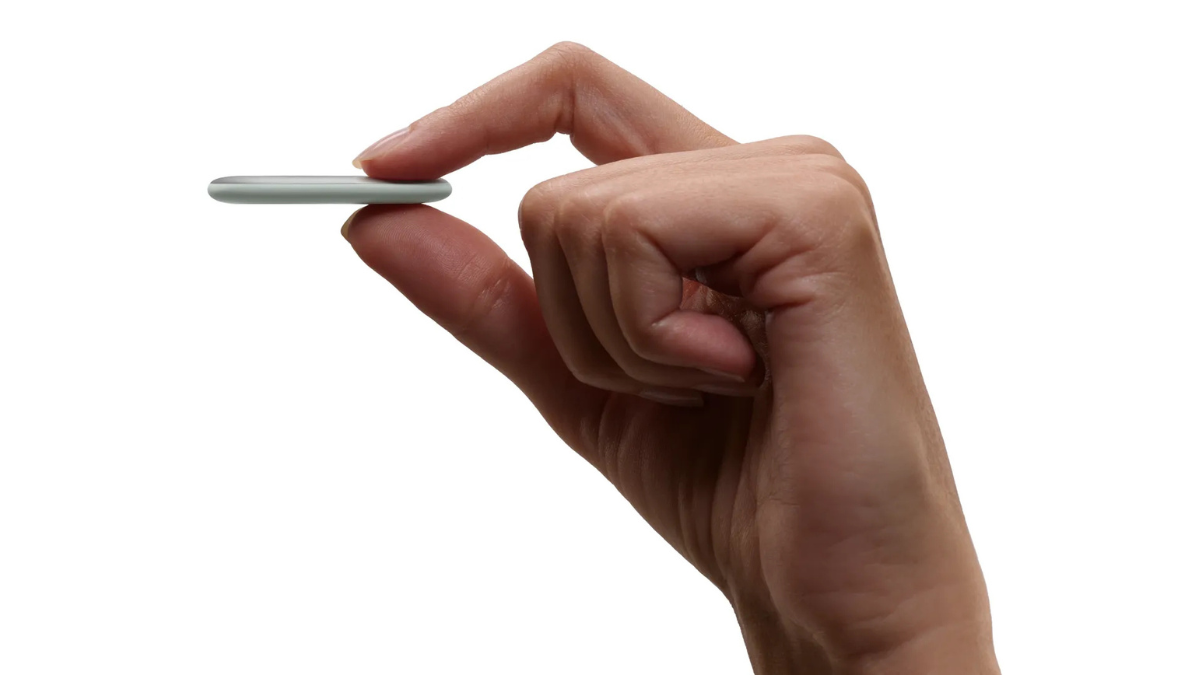 Turn-by-turn directional tracking arrives on the Google Pixel Tag 1 Hand holding thin grey oval tracker horizontally between thumb and index finger against white background hardware.