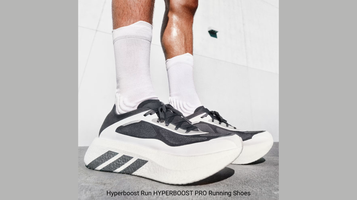Person in white socks wearing black and white Hyperboost Pro running shoes on a concrete surface runner.