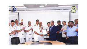 Officers in white uniforms and engineers in blue shirts on the green deck of ICGS Ajit against water vessel.