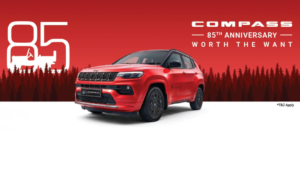 White 85 logo, red Jeep Compass 85th Anniversary Edition SUV with black roof, forest tree silhouettes background.