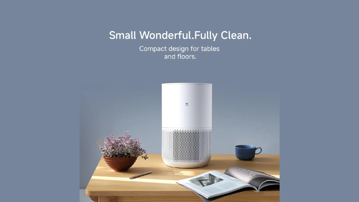 PentaClean technology debuts in the new Mijia Smart Air Purifier 6 1 Potted plant, open magazine, white cylindrical air purifier, and blue cup on a wooden table indoors.