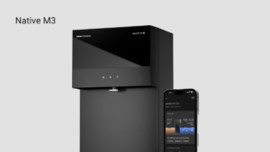 Matte black Native M3 water purifier with touch icons beside a smartphone showing water metrics in India.