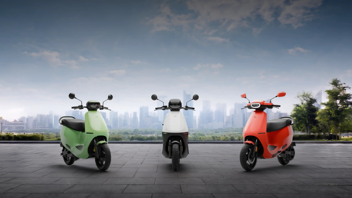 Green, white, and red scooters on an outdoor paved patio in front of trees and a distant skyline backdrop.