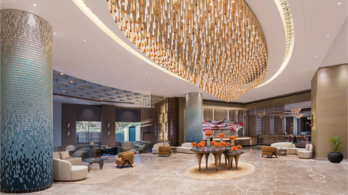 Panchkula gets India's first Vignette Collection hotel 1 Blue mosaic pillar on left, flower vases on central tables, hanging glass light installation above, hotel lobby.