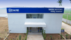 Potted plants around stairs leading into a white building below blue Tata Motors Re.Wi.Re signage in Patna.