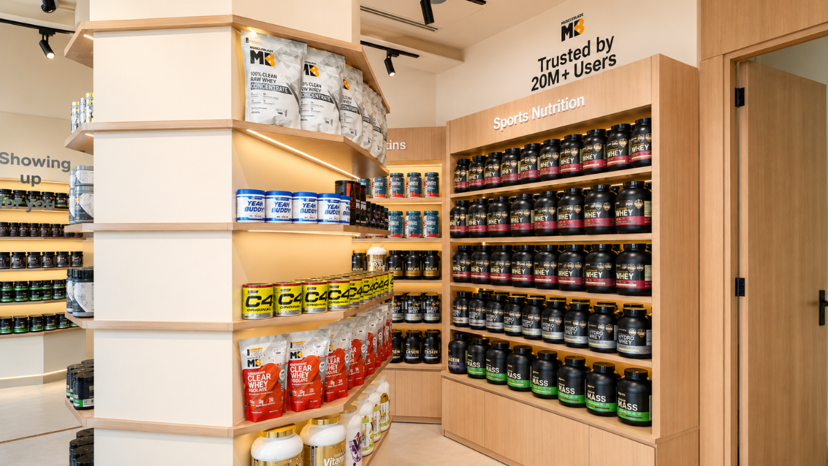 Two supplement outlets open in Dubai as HealthKart expands 1 Curved wooden shelf with supplement bags beside tall display rack filled with black whey protein tubs interior.
