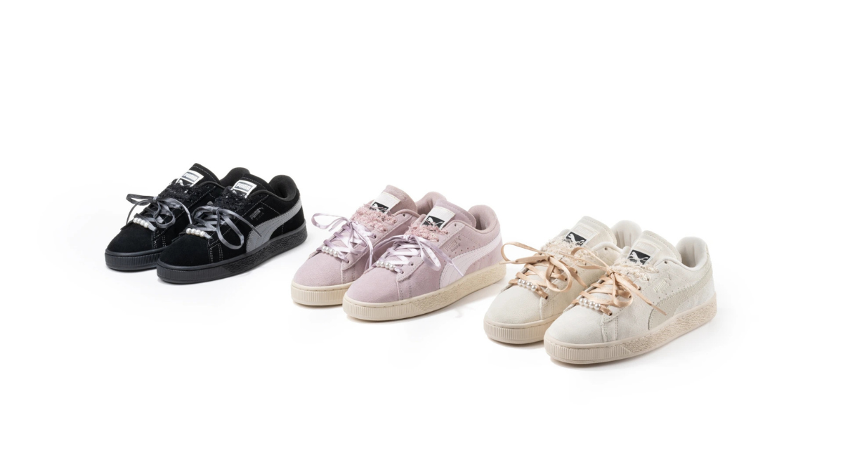 Faux pearls soften a 1968 streetwear icon 1 Black, pink, and cream low-top suede shoes with pearl beads along the laces on a white background product.