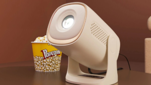 Yellow popcorn tub beside a cream Zeb-PixaPlay 72 Plus projector tilted upward on a brown surface setup.