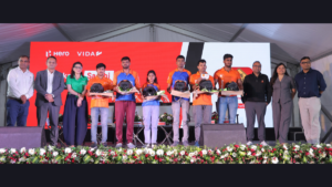 Behind front flowers, officials flank Swiggy delivery partners holding helmets on stage before a red Hero backdrop.