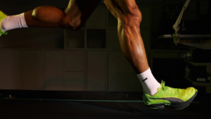 A runner strides forward, left leg raised and right foot landing in a neon FAST-R NITRO Elite 3 shoe on a dark track.
