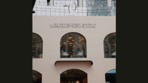 Silver Mercedes-Benz Studio lettering sits above arched glass windows showing seating and warm ceiling lights inside.