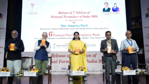 Five officials on a stage holding orange copies of the National Formulary of India 2026 before a backdrop.