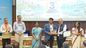 Officials standing on stage holding a trophy and award certificate before an India Electric Mobility Index screen.