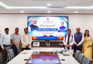 Three men, a screen showing the NIOS Bridge Course, Shri Pralhad Joshi, and two officials around a conference table event.