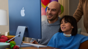 Blue monitor, keyboard, child in blue, and man before balloons, using the Screen Time safety suite. Lifestyle.