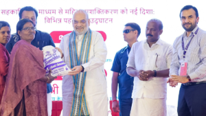 Woman in pink saree receiving an NCCF seed bag from Amit Shah beside officials at She-Mart event.
