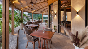 Banana plants, wooden dining sets, and glass doors with wall lamps at Taj Tadoba Resort & Spa, Nagpur, terrace.