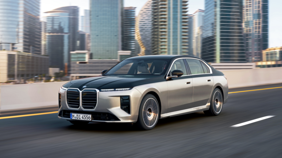 Flagship 7 Series range arrives in India from Rs 1.95 crore 1 A two-tone sedan drives forward along a highway in the foreground, with tall glass skyscrapers in the background.