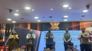 Five officials standing on stage before a large screen displaying the emblem of India at the CAG-BHASHINI Anuvaad ceremony.
