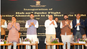 Officials clapping behind floral arrangements on stage before a backdrop for the hub and spoke aviation framework launch.